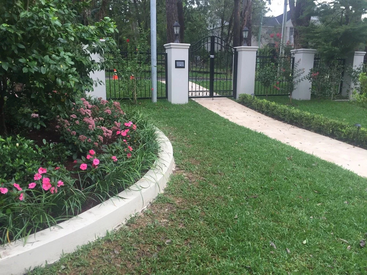 Curved garden bed with pink flowers and banded lawn edging beside the Warrawee pedestrian gate