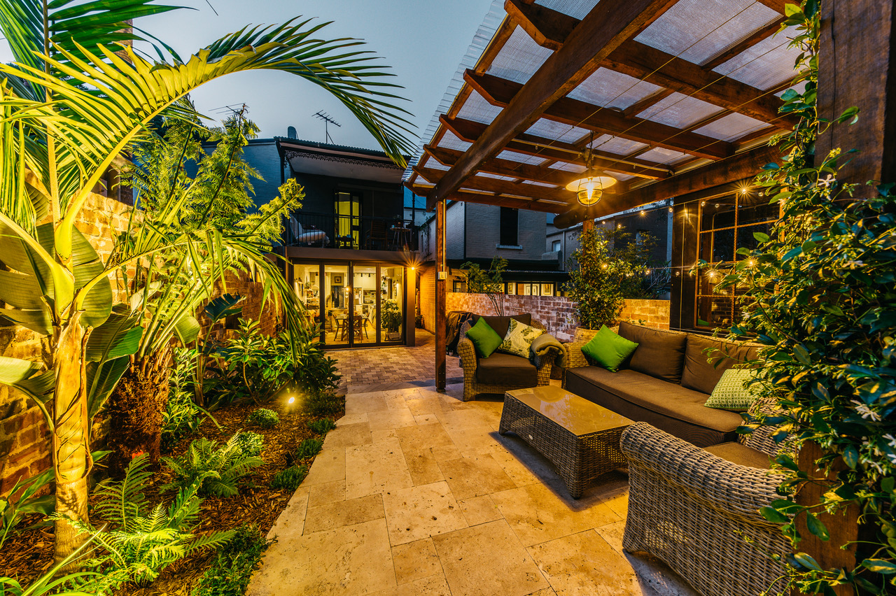 Glebe courtyard at night with covered lounge seating, tropical planting and landscape lighting