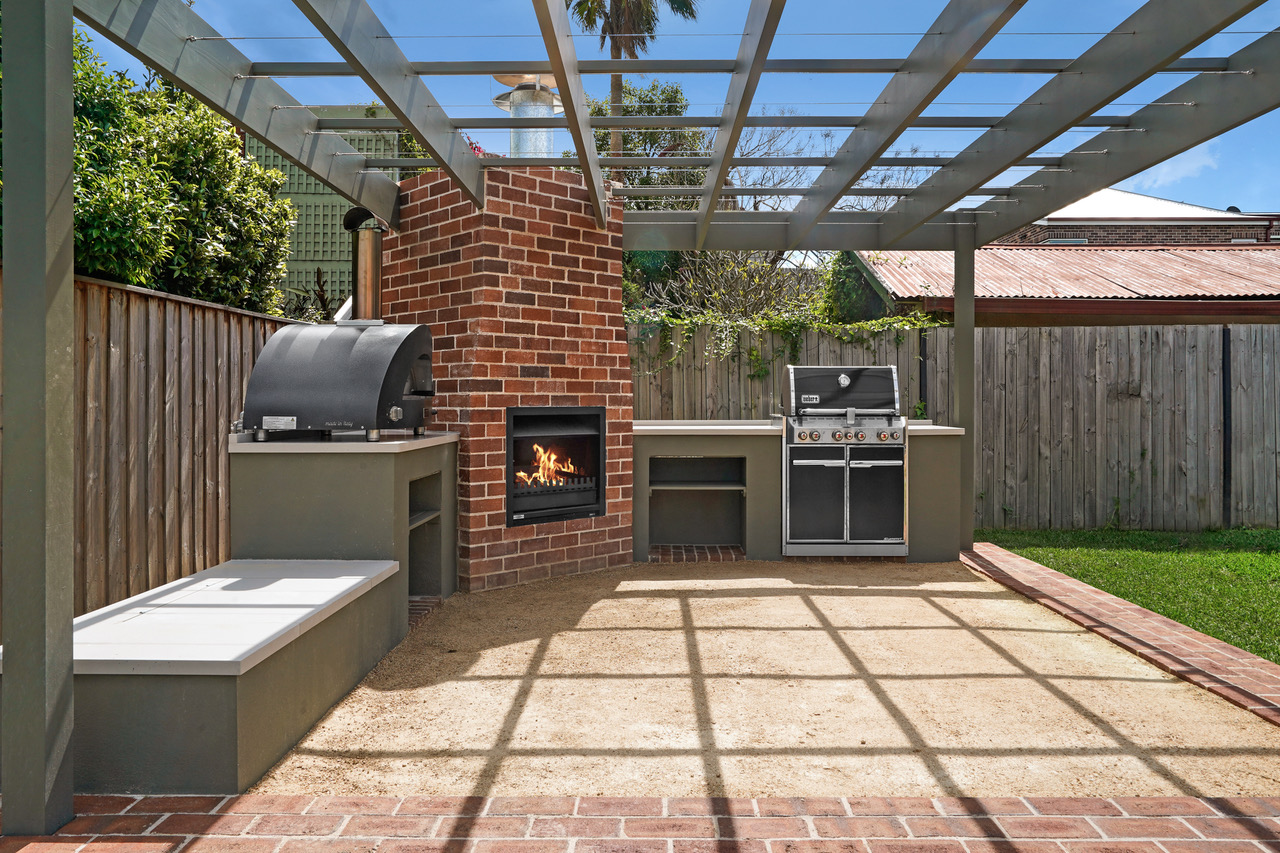 Outdoor kitchen, pizza oven and fireplace beneath an open steel pergola
