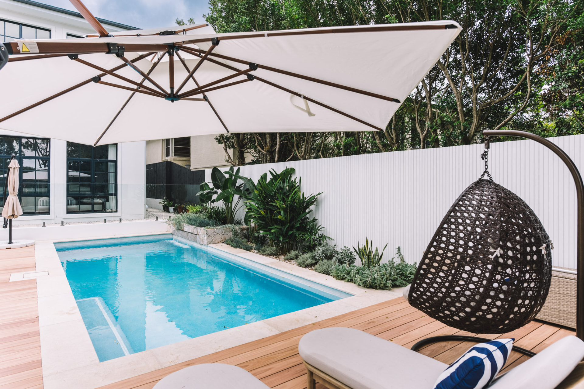 Completed Chatswood pool beneath a cantilevered umbrella with hanging egg chair and tropical planting