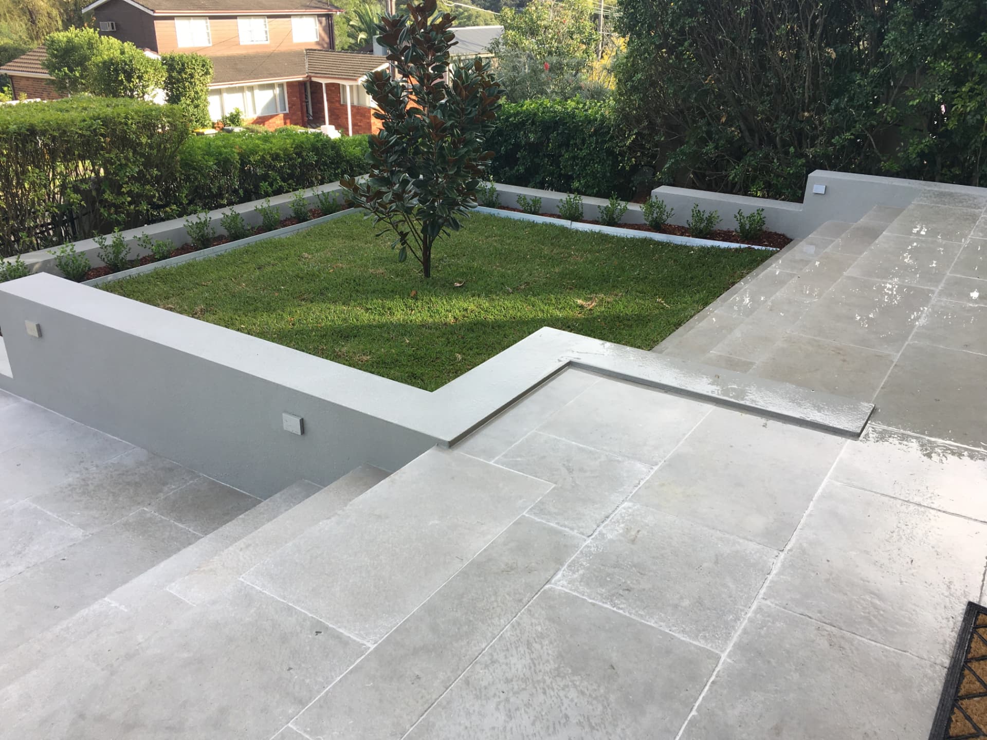 Level lawn garden with rendered planter walls, spotlighting and paved steps at Riverview