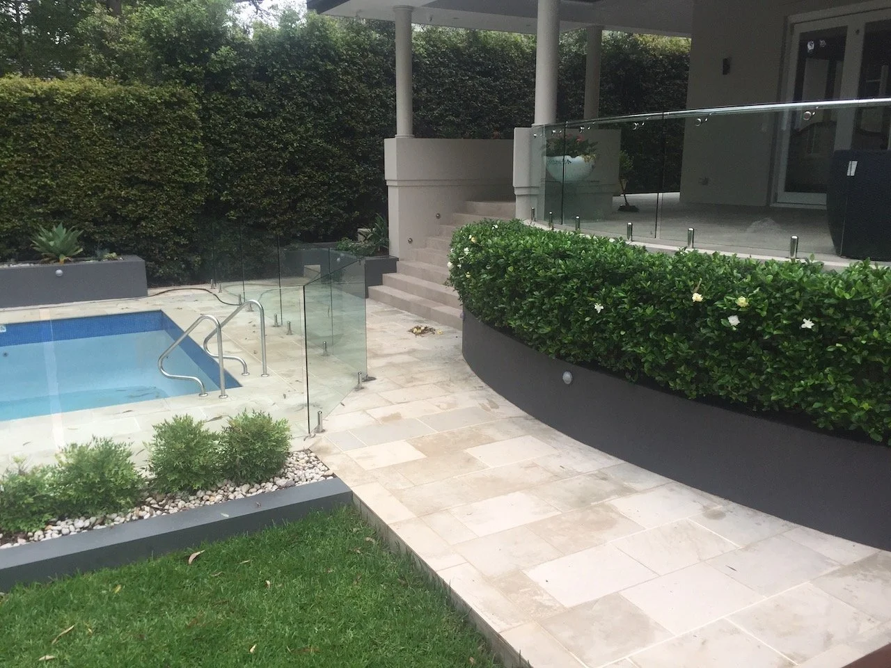 The renovated Warrawee pool with frameless glass fencing, curved planter wall and paved terrace