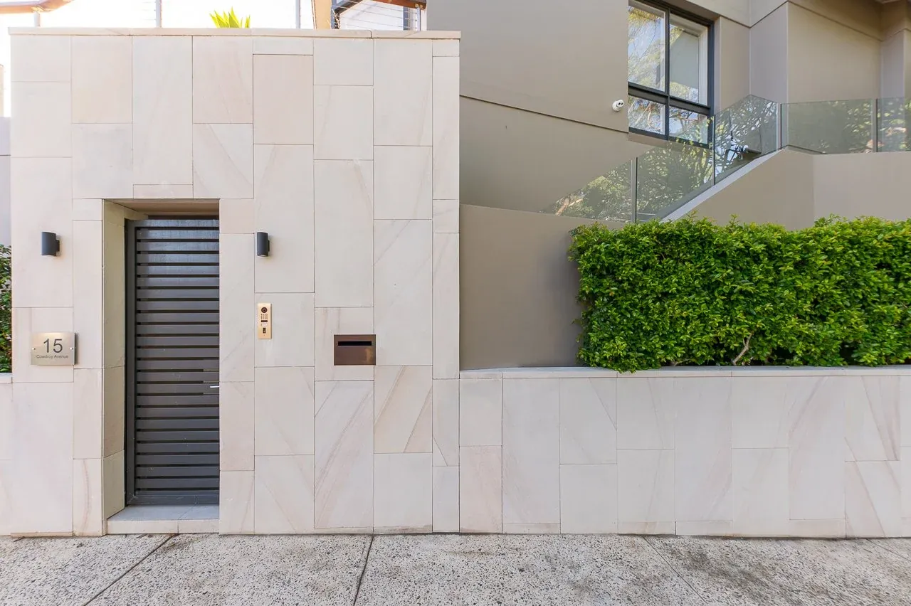 Sandstone-clad front entrance with slatted privacy gate, intercom and integrated letterbox