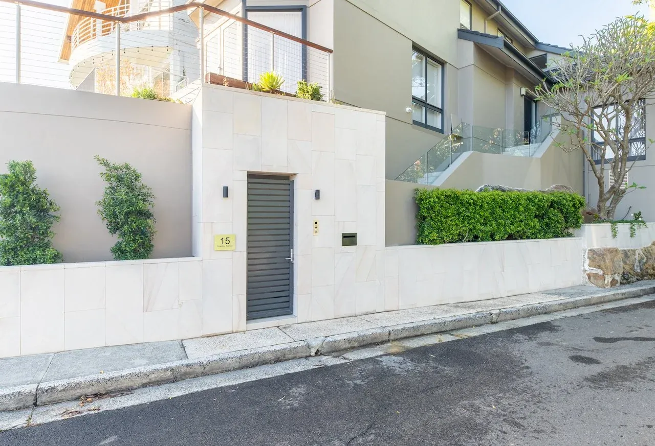 Entry elevation from the street showing sandstone cladding, hedge planter and glass balustrade