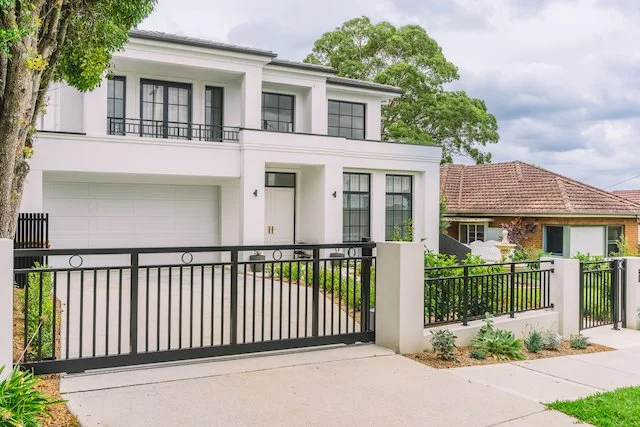 Chatswood front driveway with sliding steel gate, rendered piers and hedged garden beds