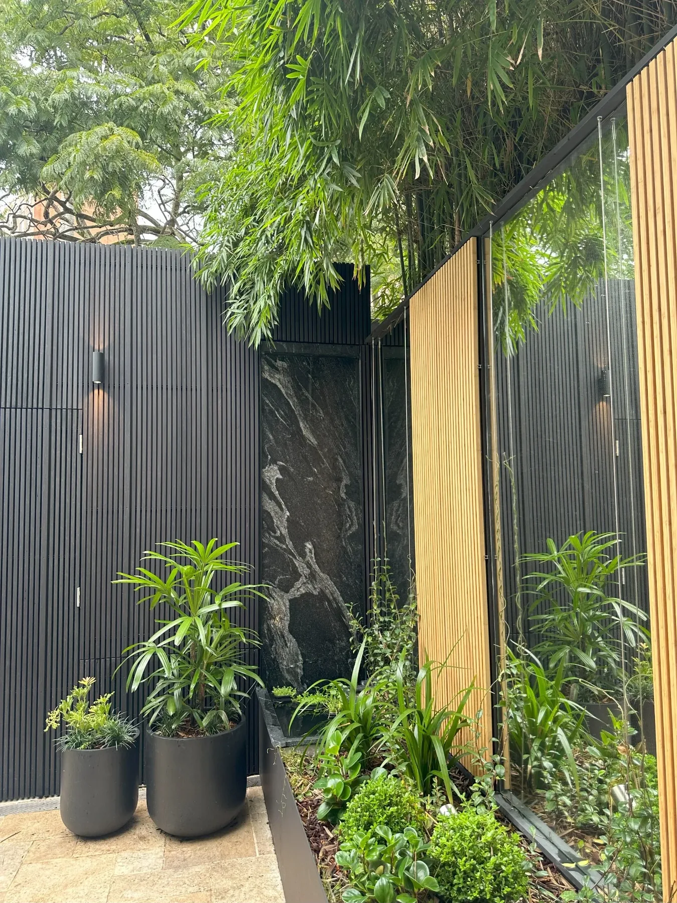 Stone water feature framed by black battened screens, timber cladding and layered planting