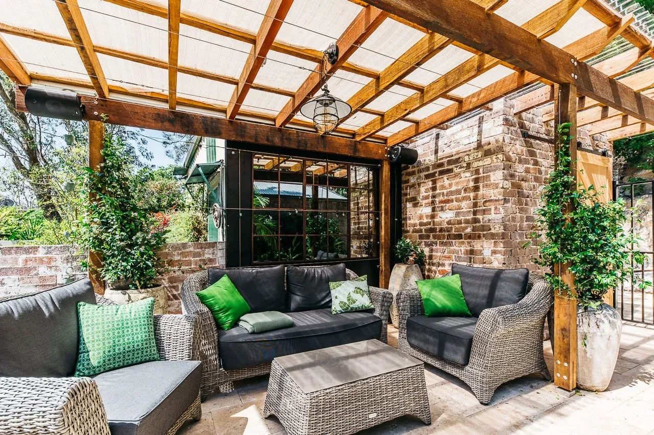 Wicker lounge setting beneath the hardwood pergola against original recycled brick walls