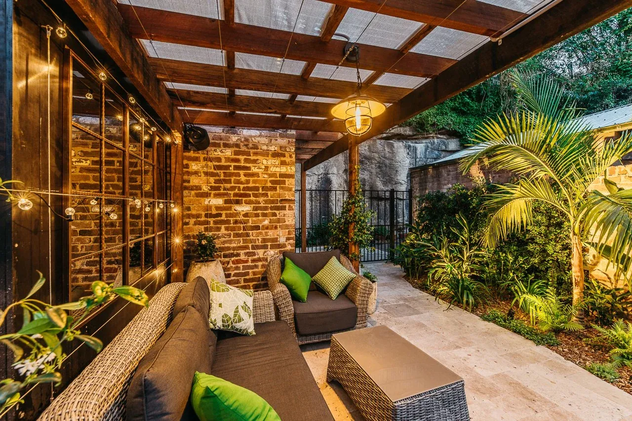 Evening lighting under the pergola with warm pendant, festoon strings and uplit palms