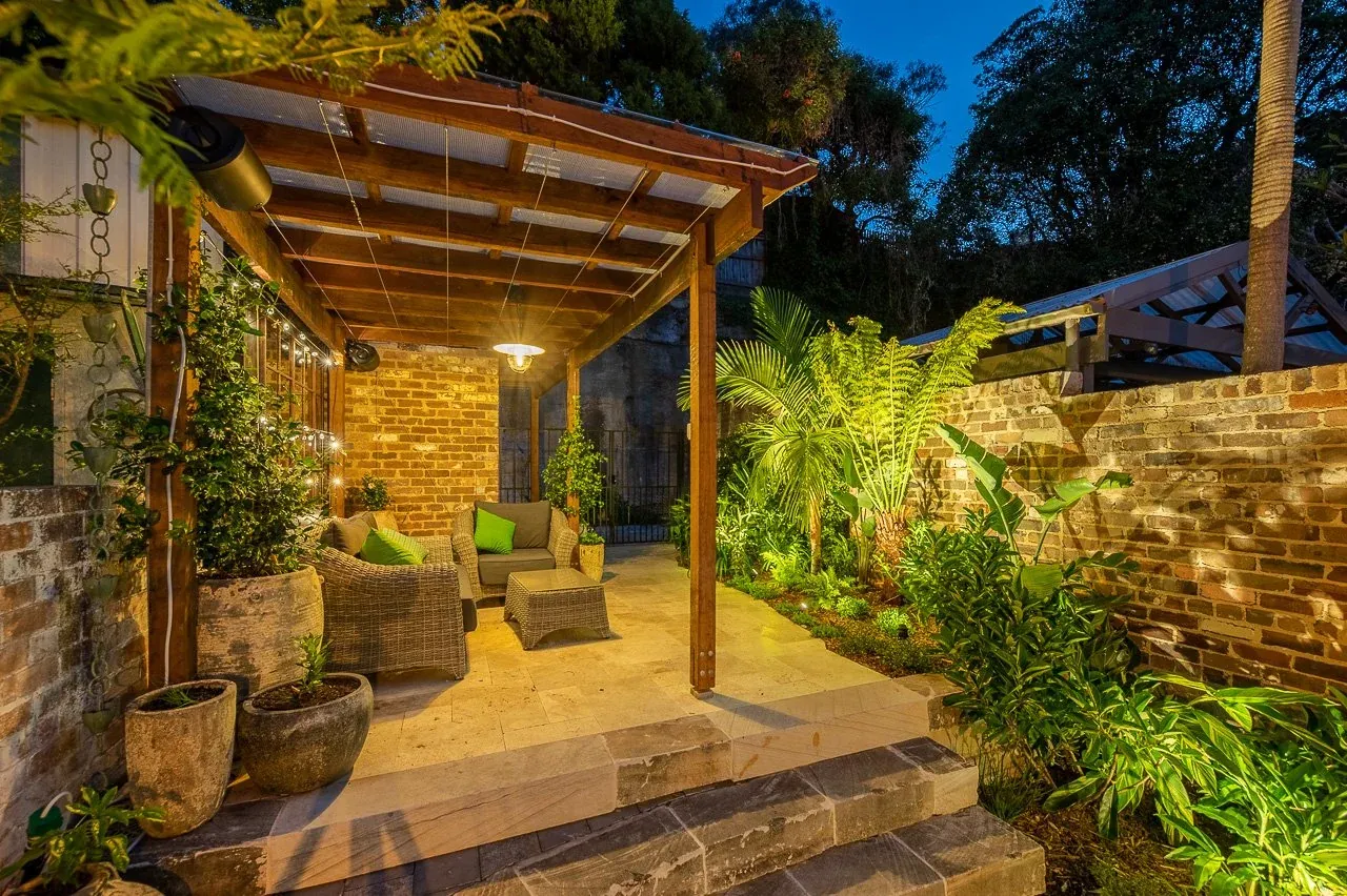 Sandstone steps and travertine landing lit at night beside the planted courtyard edge