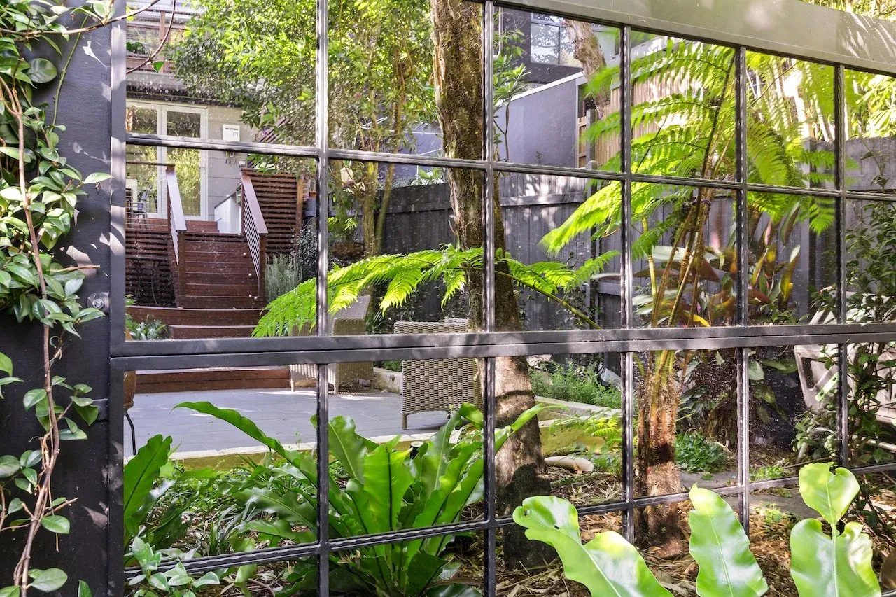 Steel-framed feature garden mirror reflecting tree ferns and courtyard planting