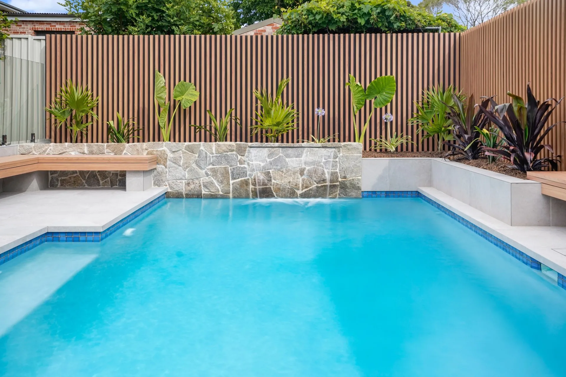 Tiled pool with dry-stack stone waterfall wall and timber batten screen