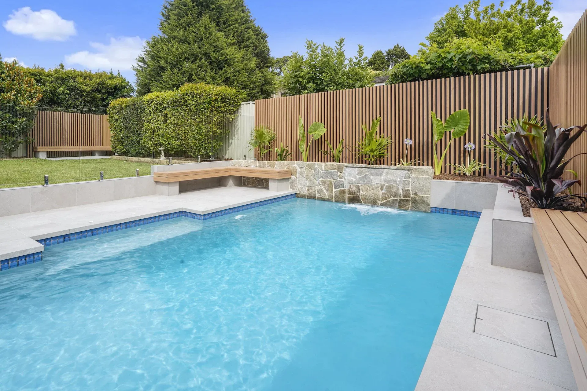 Renovated pool with stone-clad water feature wall and raised planter beds