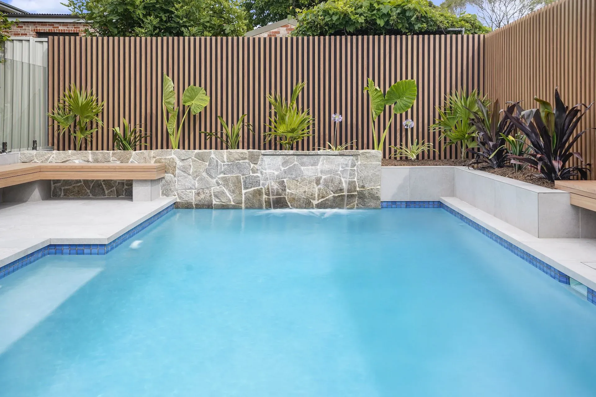 Stone-clad water wall spilling into the pool below layered planting
