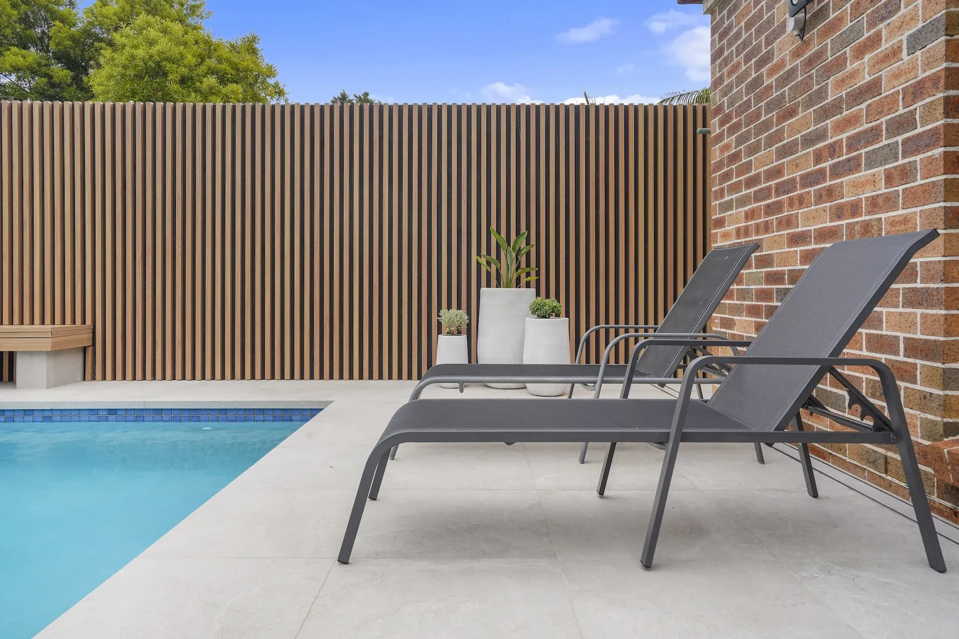 Sun loungers on the paved terrace against the battened screen and brick wall