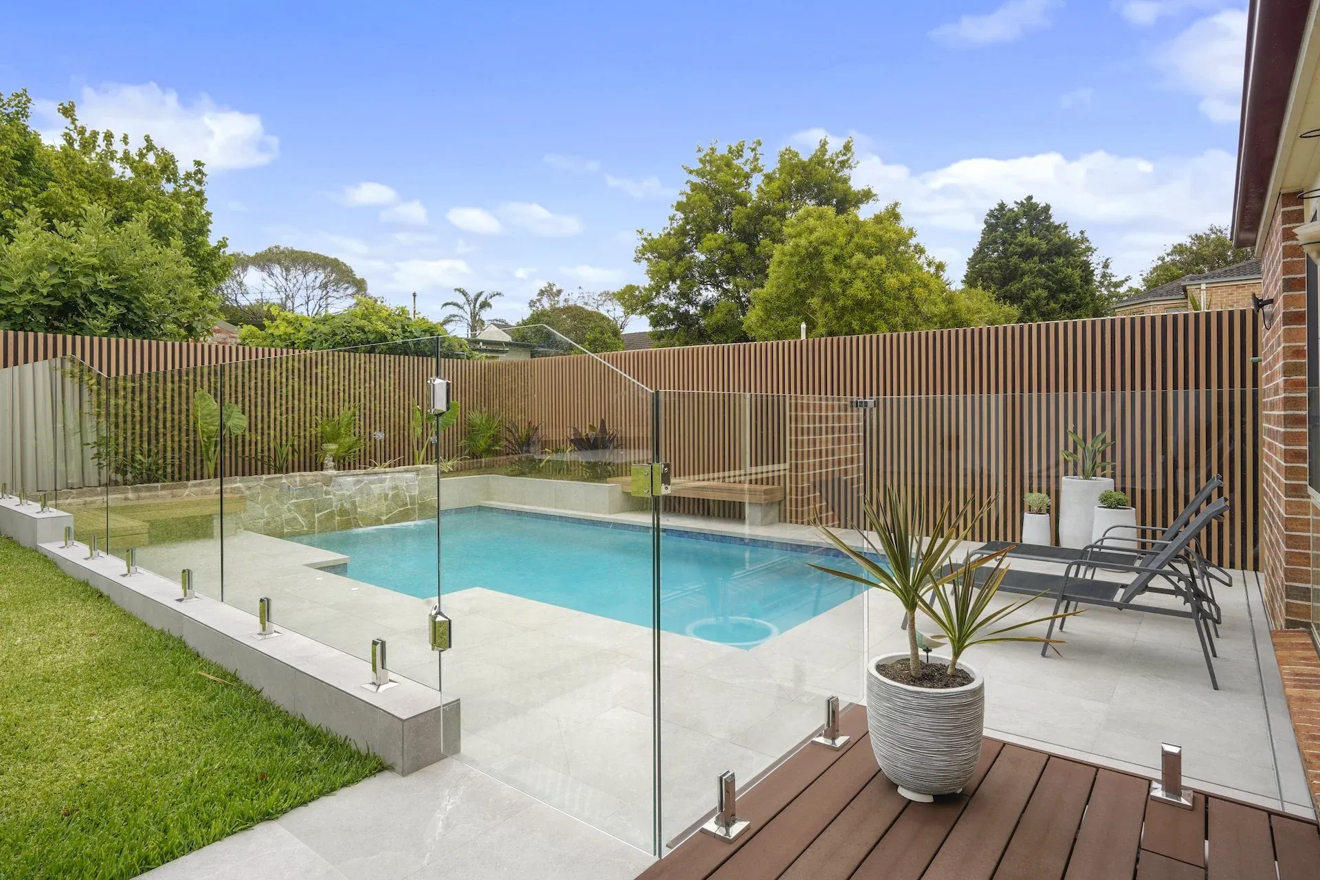 Frameless glass pool fencing separating the lawn from the paved pool terrace