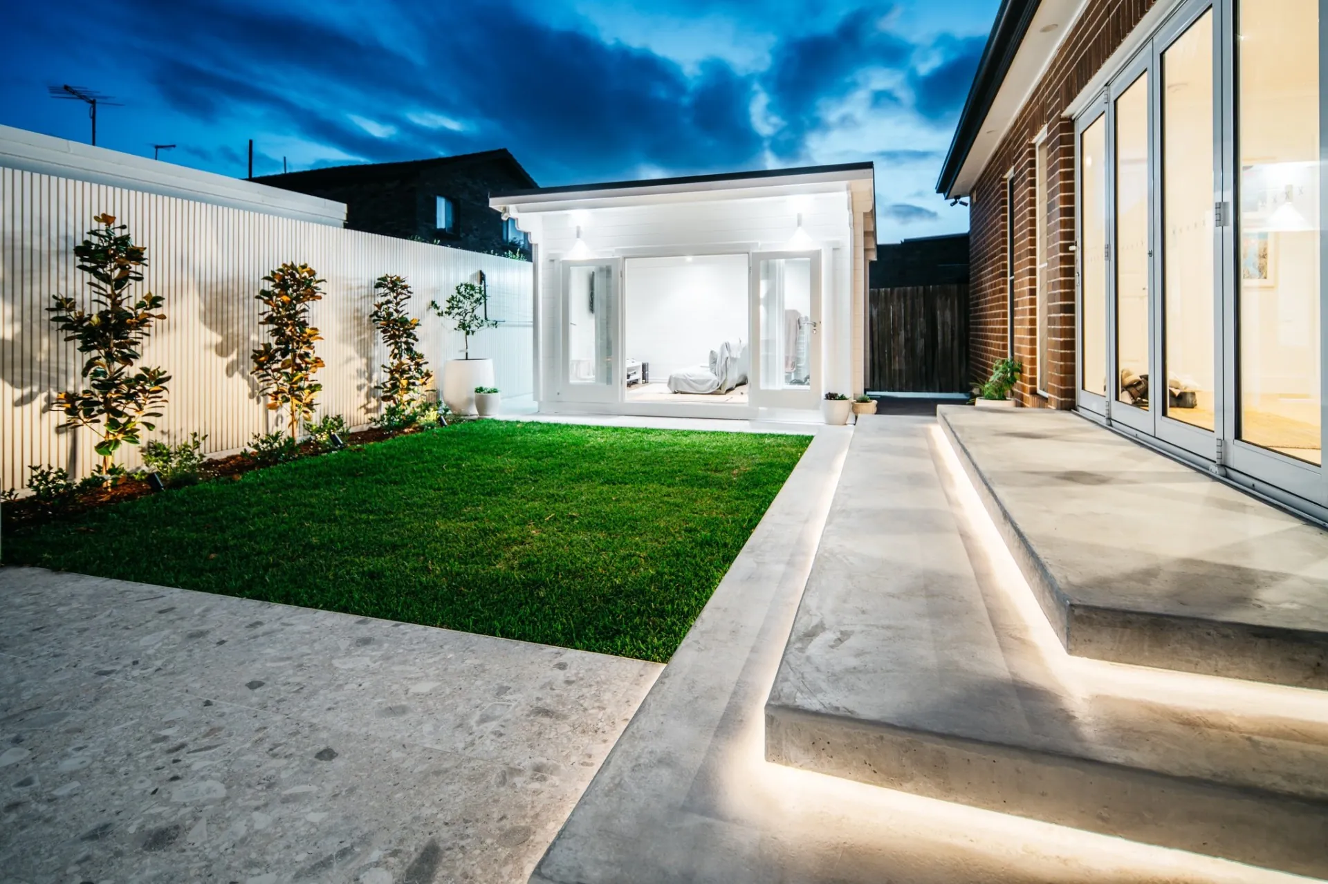 Manicured lawn, concrete terrace and LED step lighting at twilight
