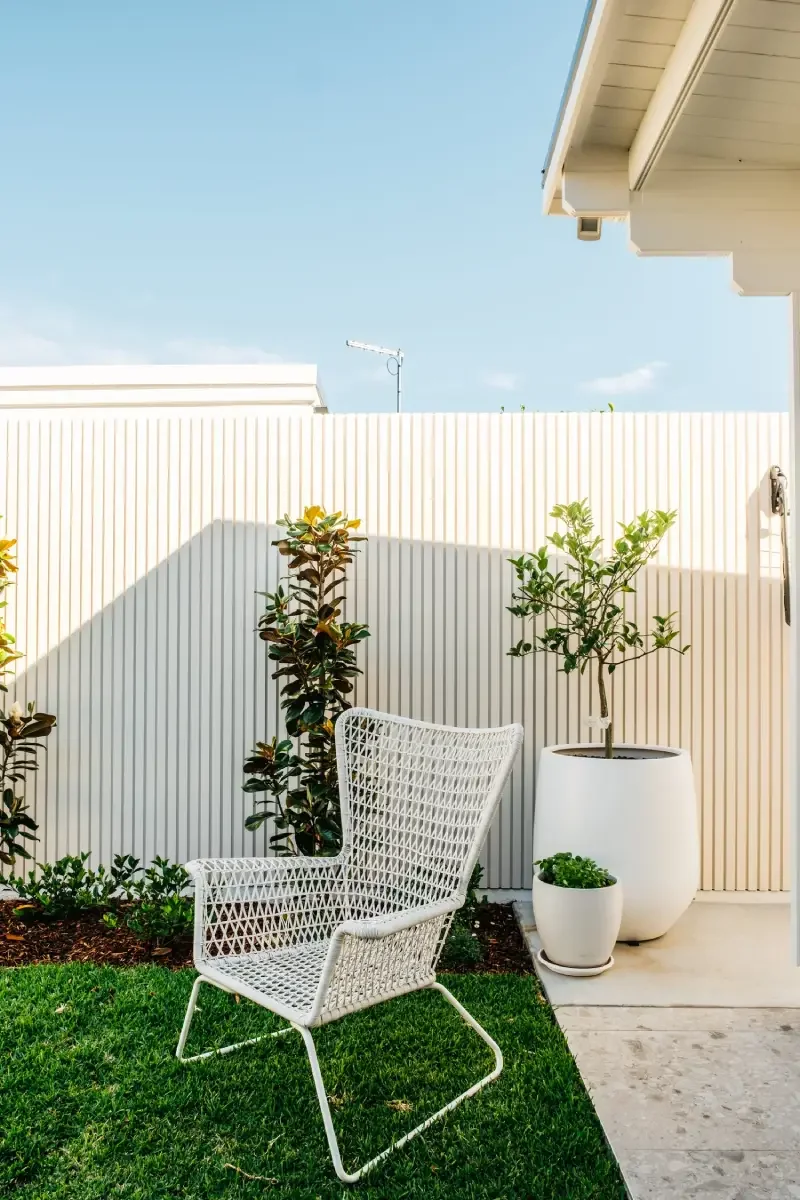 Wicker chair on turf beside vertical batten screening and potted citrus in Russell Lea