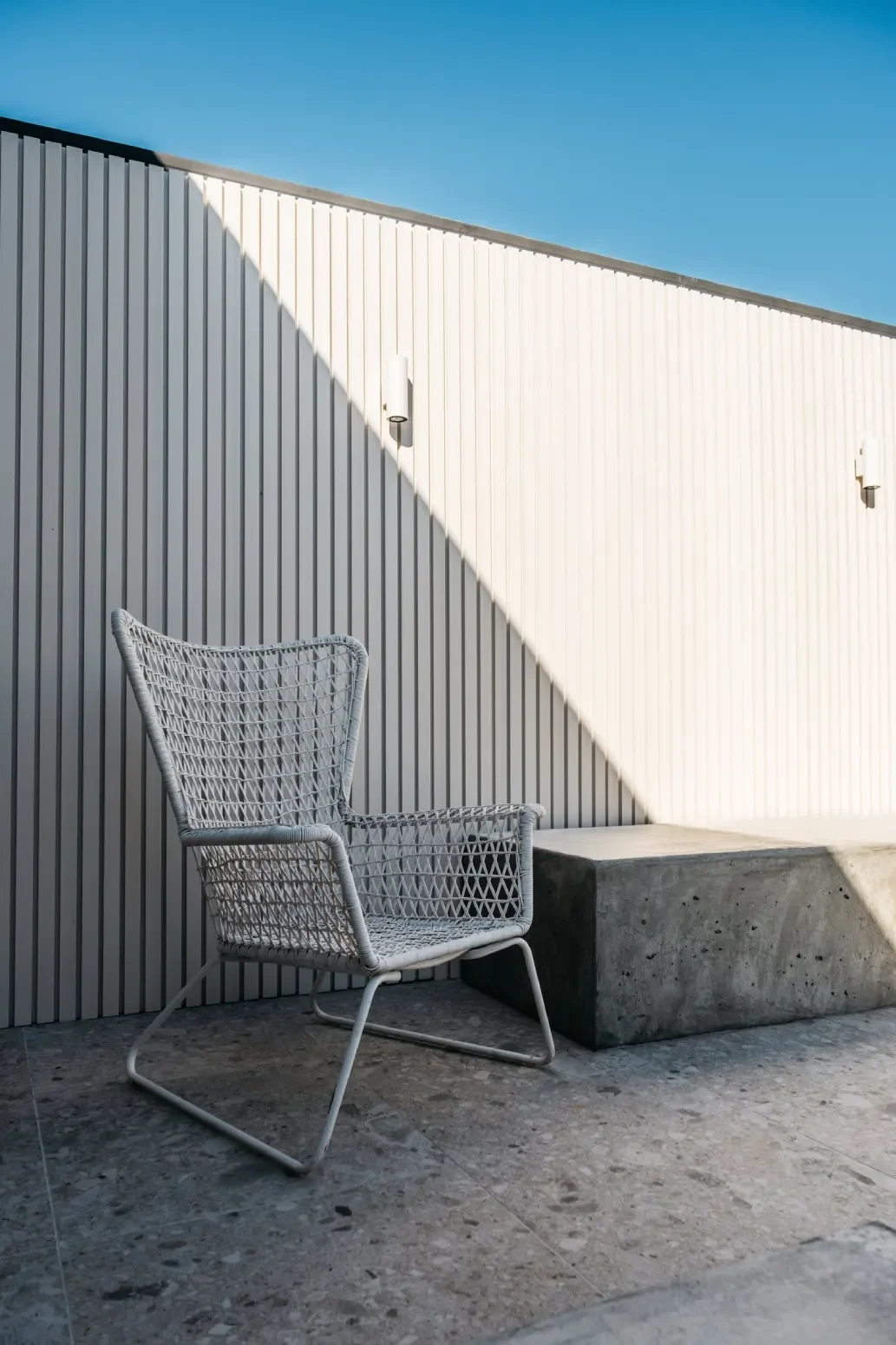 Wicker chair against battened wall with board-formed concrete bench and terrazzo paving