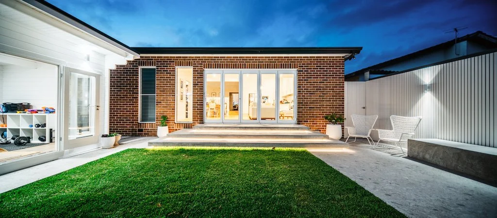 Dusk panorama of the Russell Lea courtyard with lit steps, turf lawn and cabin