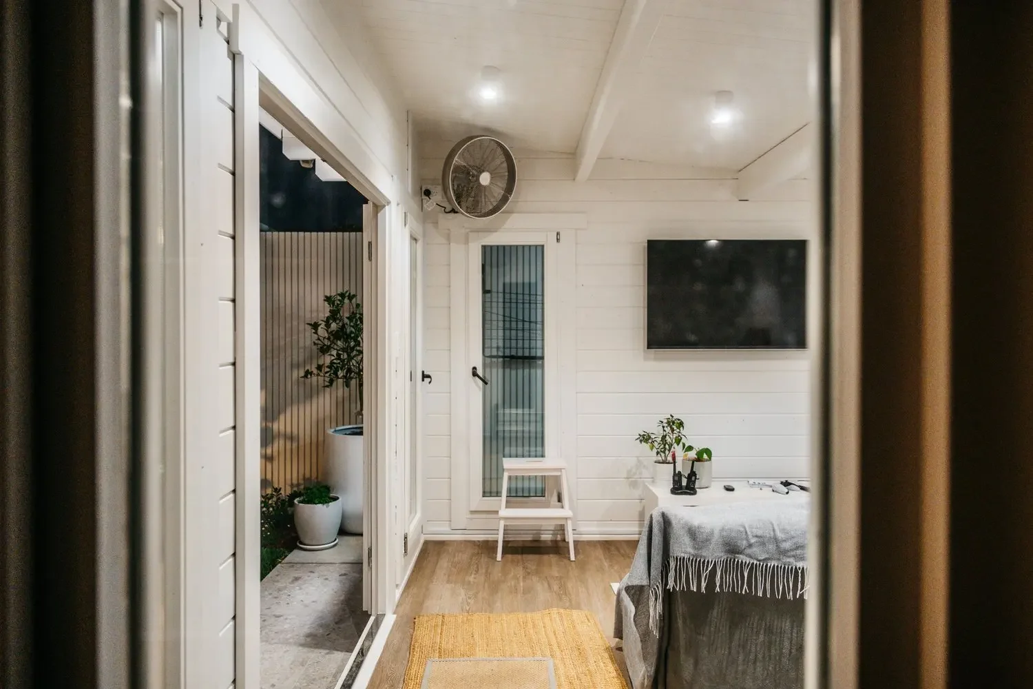 View through the cabin doorway at dusk with wall fan, downlights and timber flooring