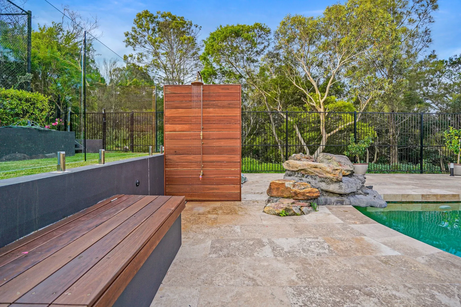 Outdoor shower and bench seat beside the pool with feature rock wall