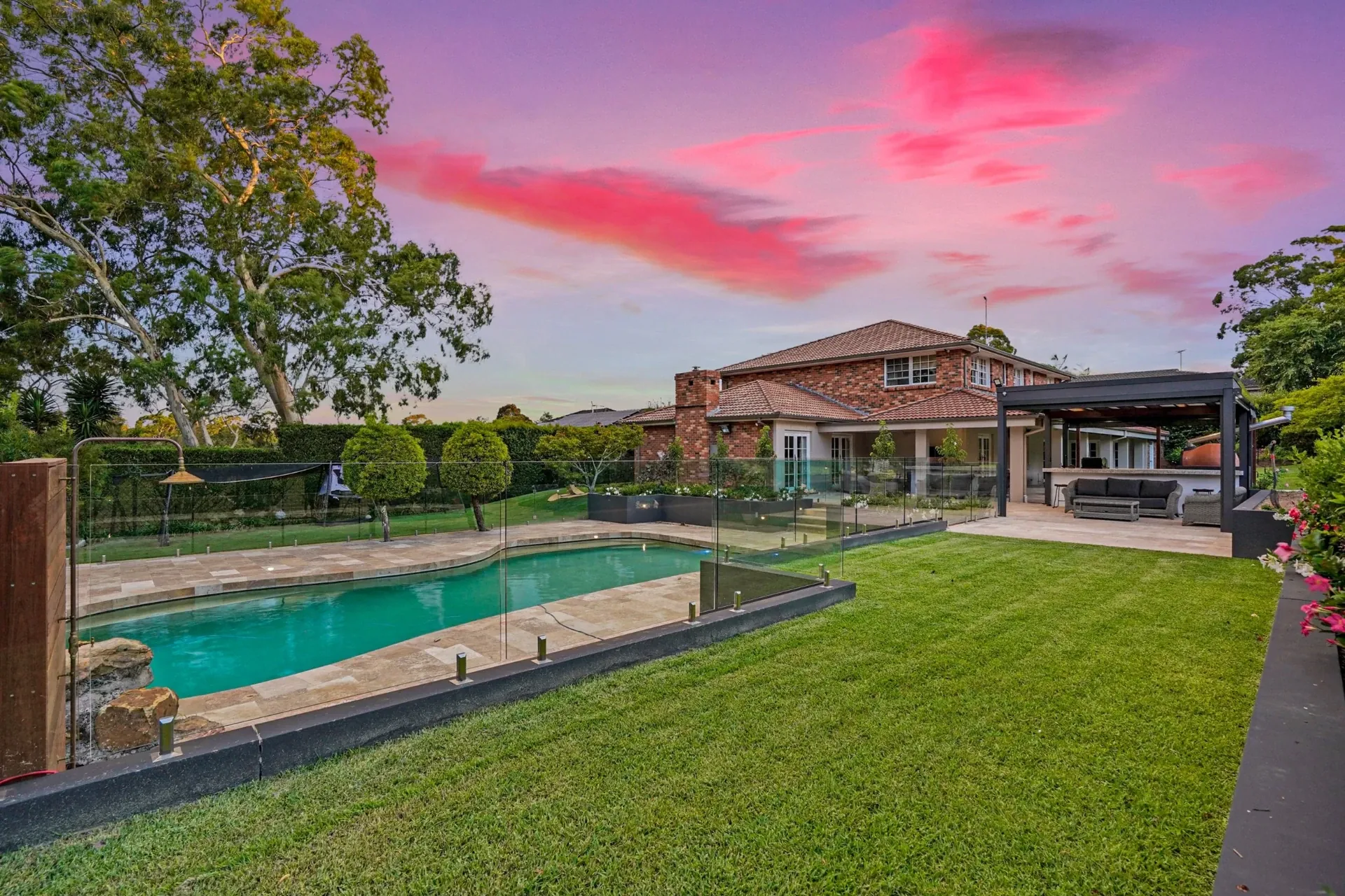 Level lawn, glass pool fencing and pool terrace at dusk with the house beyond