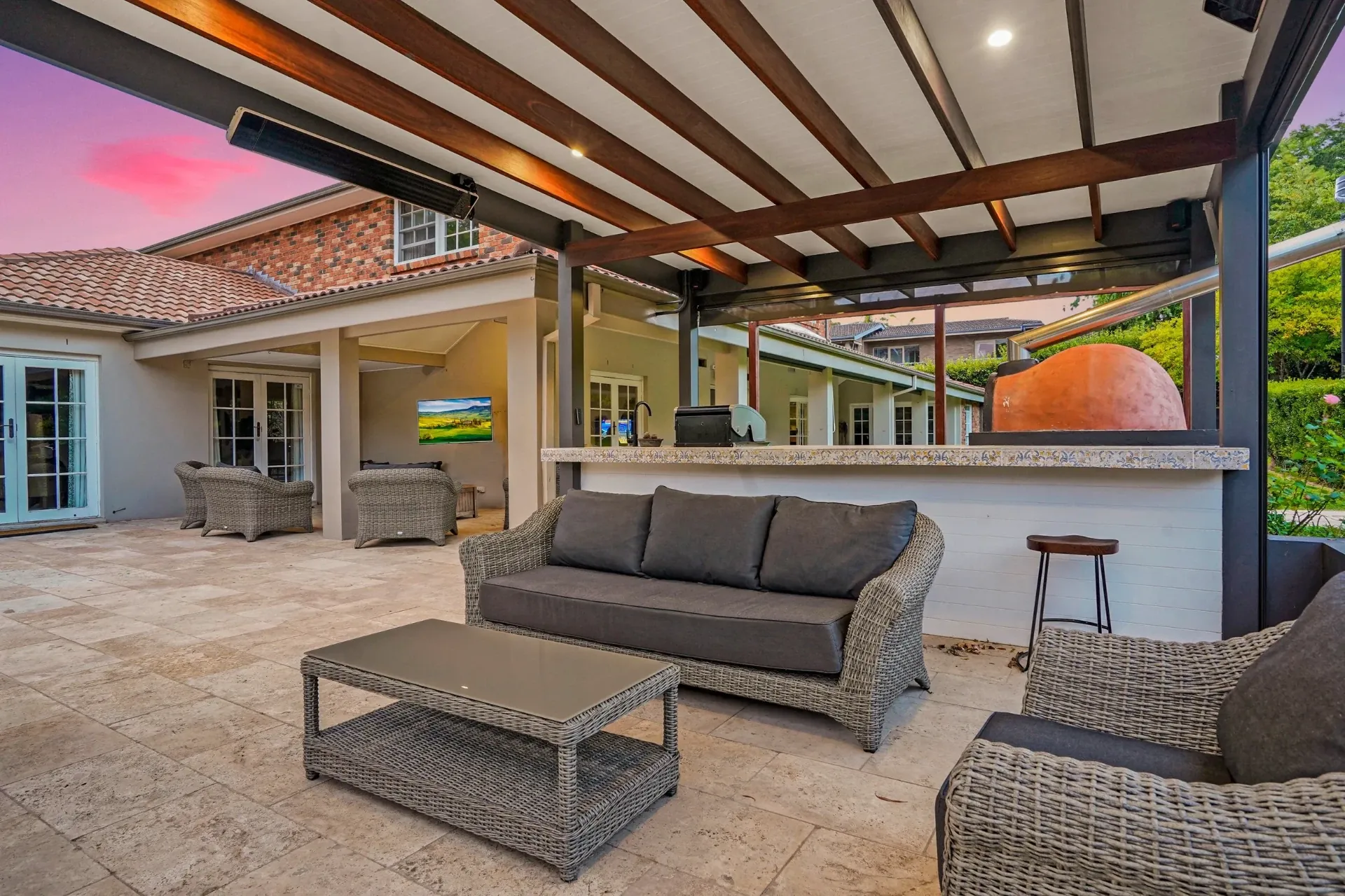 Pergola bar with bench seating and wood-fired pizza oven at dusk